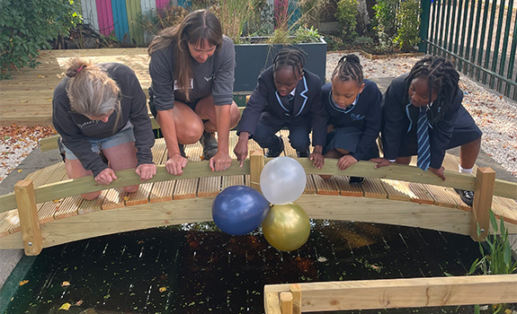 Teachers and children crouching on the bridge, looking into the new pond at St Luke's funded by F.B.Coales No.4 (Family) Trust